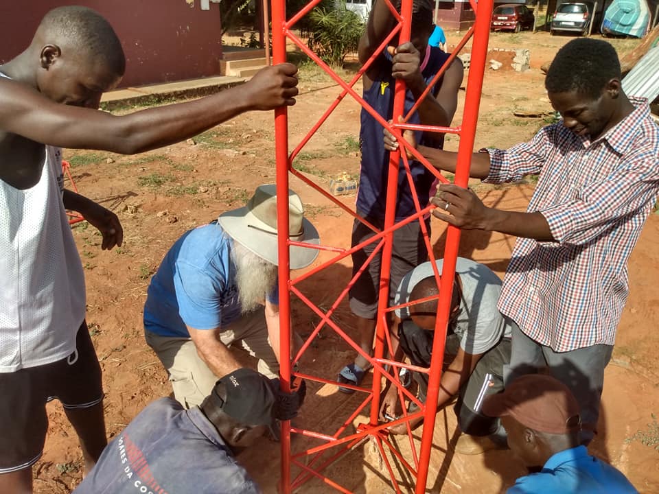 A Galcom technician and local partners raising a red radio tower section together